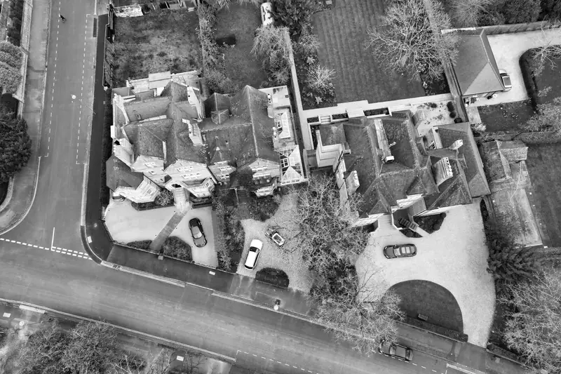 Aerial view of large detached houses with hipped roofs, valleys and flat-roofed extensions among trees, the roof shapes that set the price of work in Formby