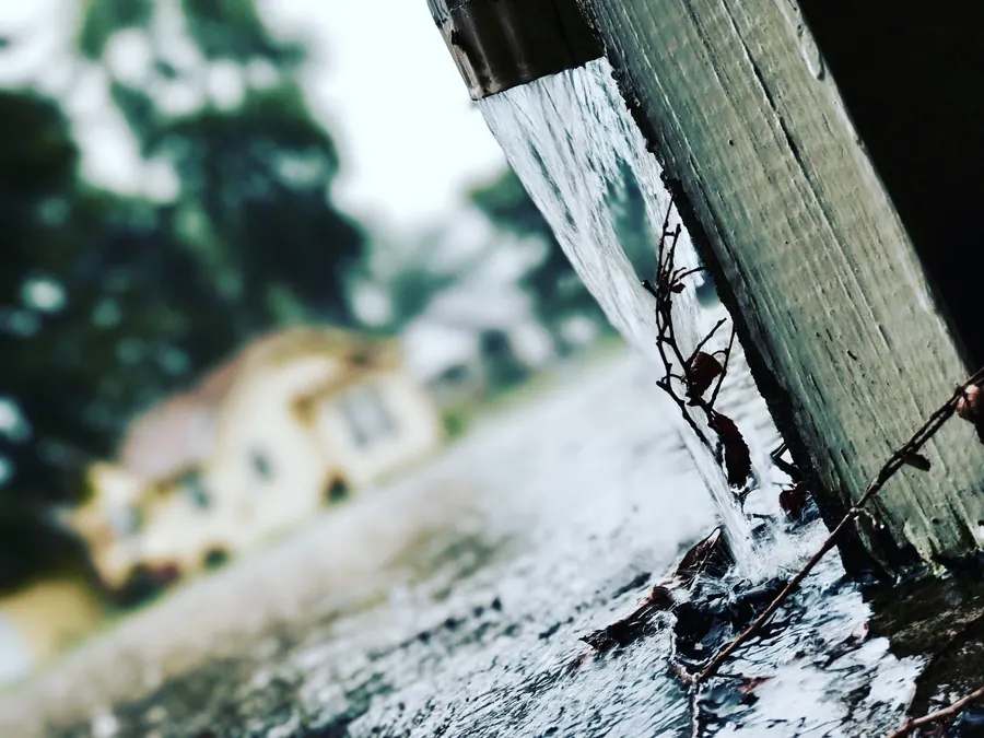 Rainwater overflowing past a blocked downpipe in heavy autumn rain, the failure gutter clearing in autumn prevents