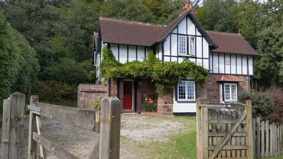 A detached mock-Tudor house with a steep tiled roof and gables, set among mature trees like the larger homes of Freshfield in Formby