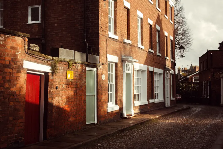 A narrow cobbled street of tall red brick town houses with a pedestrian zone sign, the kind of market-town access that shapes scaffolding in Ormskirk centre