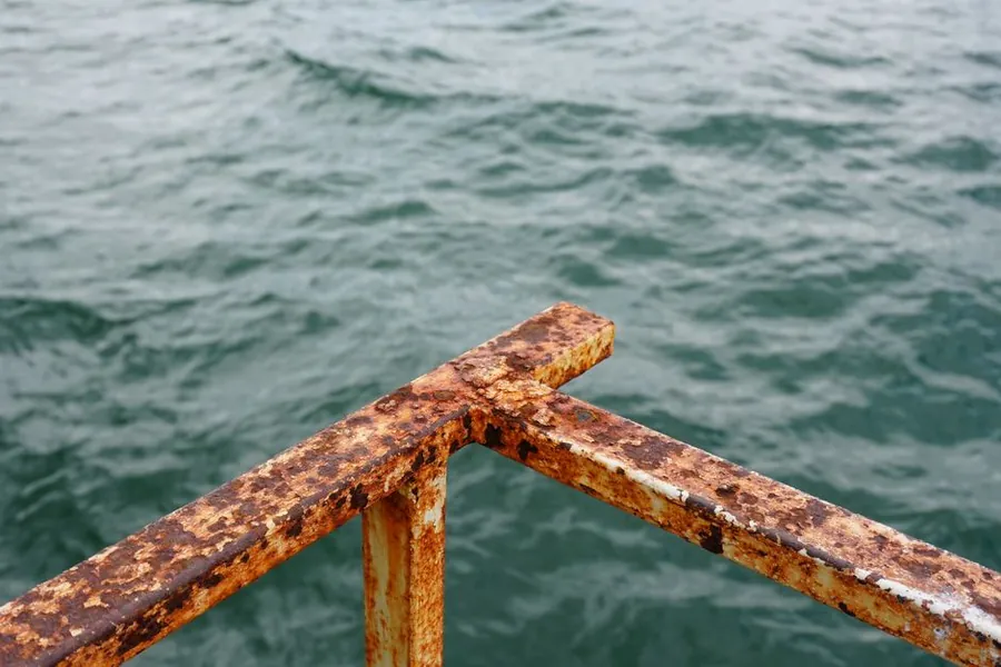 Heavily corroded metal railing against seawater, the same salt exposure Southport roof fixings face