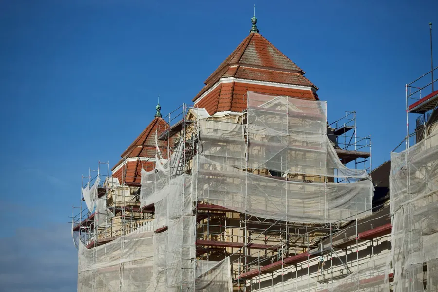 Scaffold and debris netting wrapped around a tall slate-roofed building during re-roofing