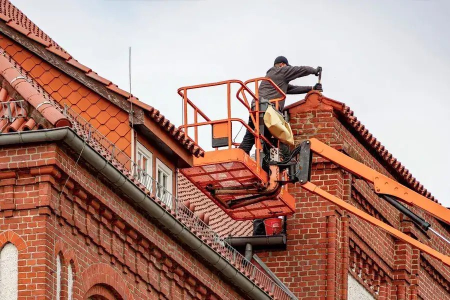 Roofer inspecting a brick property from an access platform, the kind of check worth doing each spring
