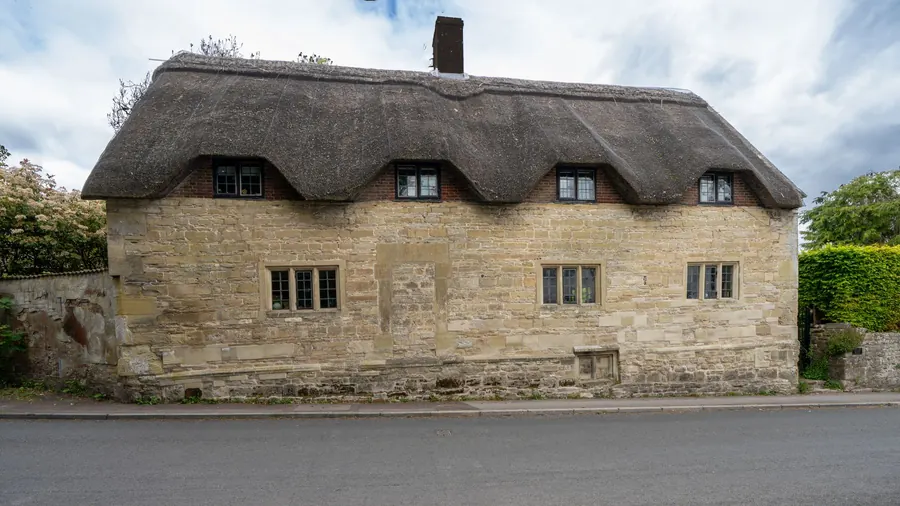 A long thatched cottage with a brick chimney beside a village road, similar to the thatched house in Formby's Green Lane conservation area