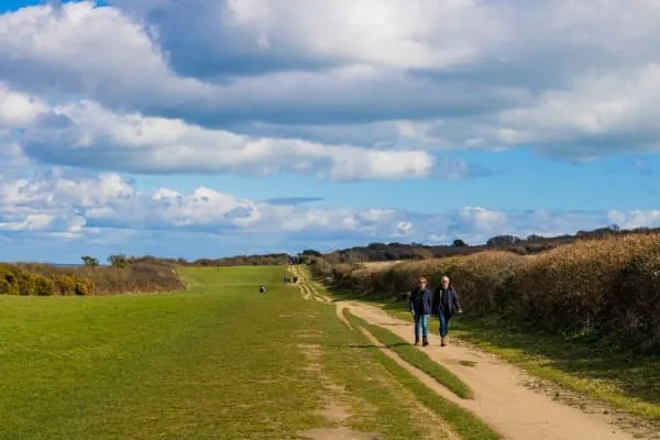 Walkers on a flat green countryside path with hedgerows, like the Cheshire Lines Path near Maghull