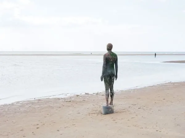 One of the cast-iron Antony Gormley figures standing on the sand at Crosby beach