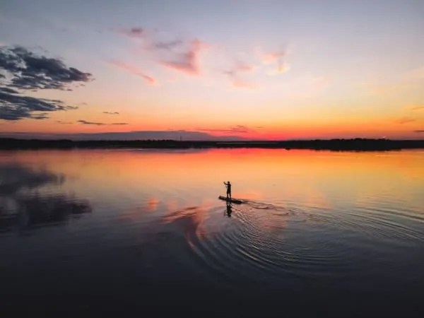 A paddleboarder crossing calm water at sunset, the kind of session run at Crosby Lakeside