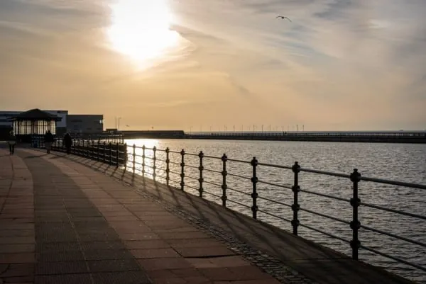 A seaside promenade with railings at golden hour, looking out over the water as at Crosby Coastal Park