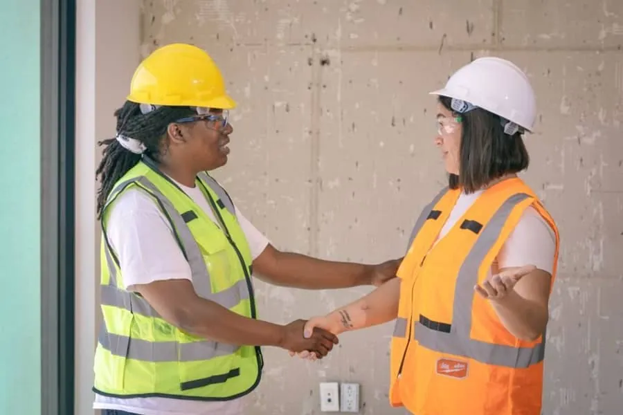 Two tradespeople in safety gear shaking hands after agreeing a job