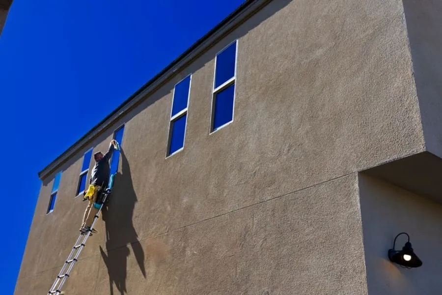 Person on a ladder clearing the gutters and roof edge of a house