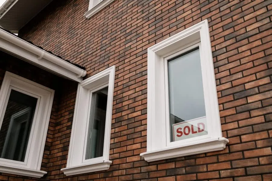 Brick house with a sold sign in the window, the point at which roof findings get renegotiated