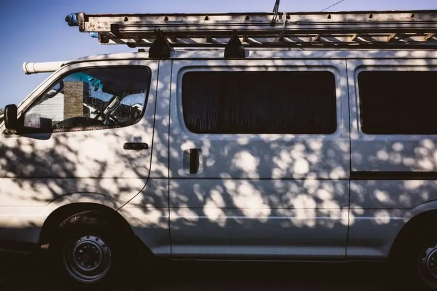 Roofing contractor's van with a ladder mounted on the roof parked outside a residential property