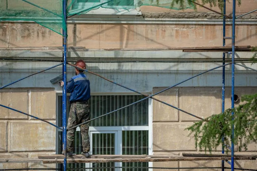 A worker on scaffolding carrying out repairs to a building facade and roof edge