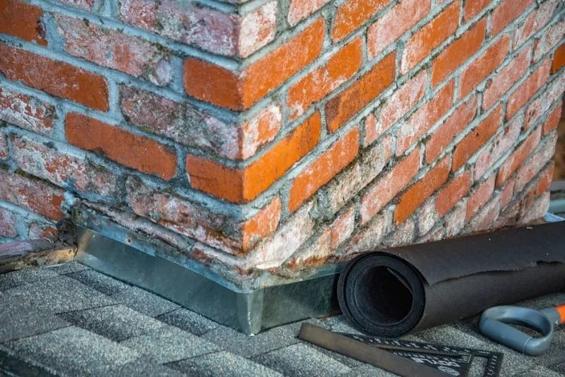 A brick chimney stack with tools and materials in place for repointing and flashing repairs
